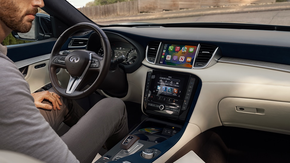 Interior of 2024 INFINITI QX50 featuring man sitting in driver seat with Apple CarPlay showing on infotainment screen
